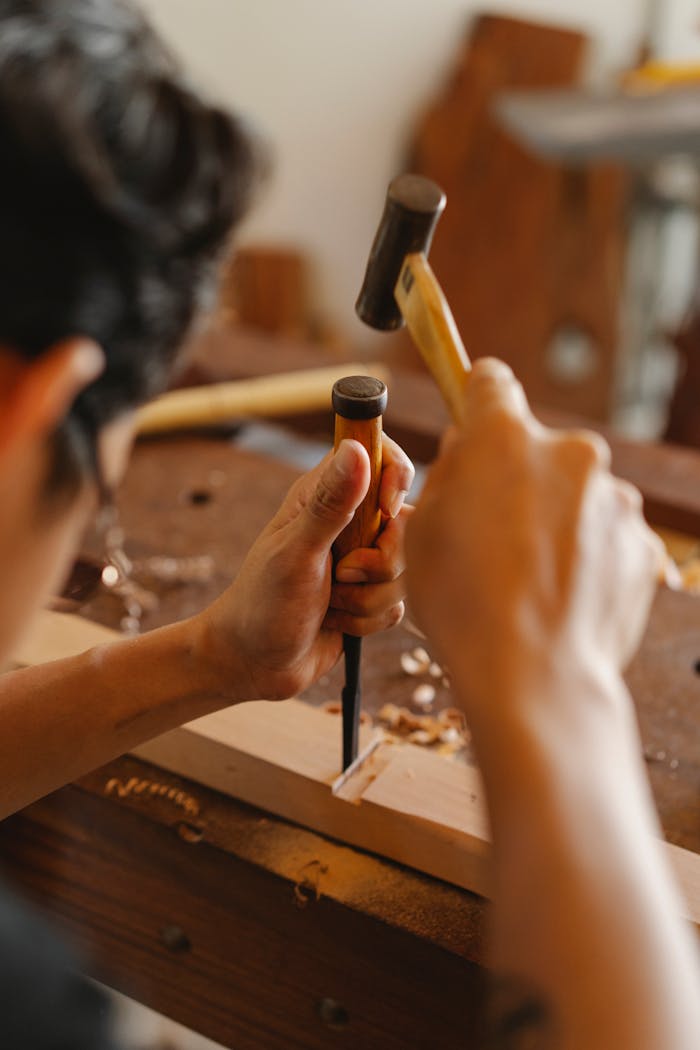 A craftsman using a hammer and chisel to carve wood in a workshop.